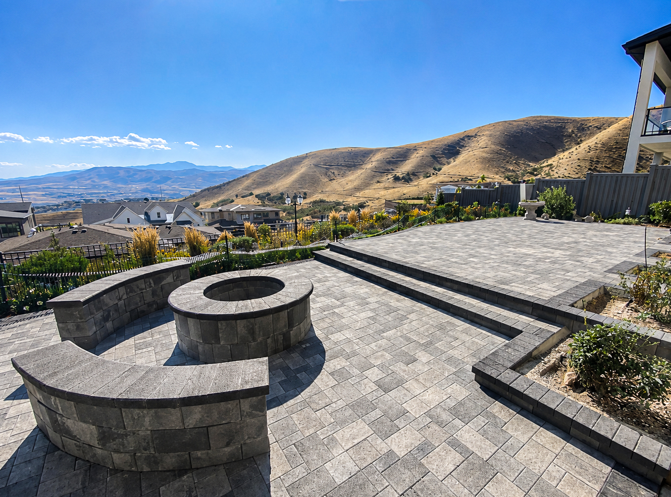 Fire Pits & Features in Utah Stone paver patio with a circular fire pit and curved seat wall overlooking Utah foothills, fire pits & features by Empire Pavers in Utah