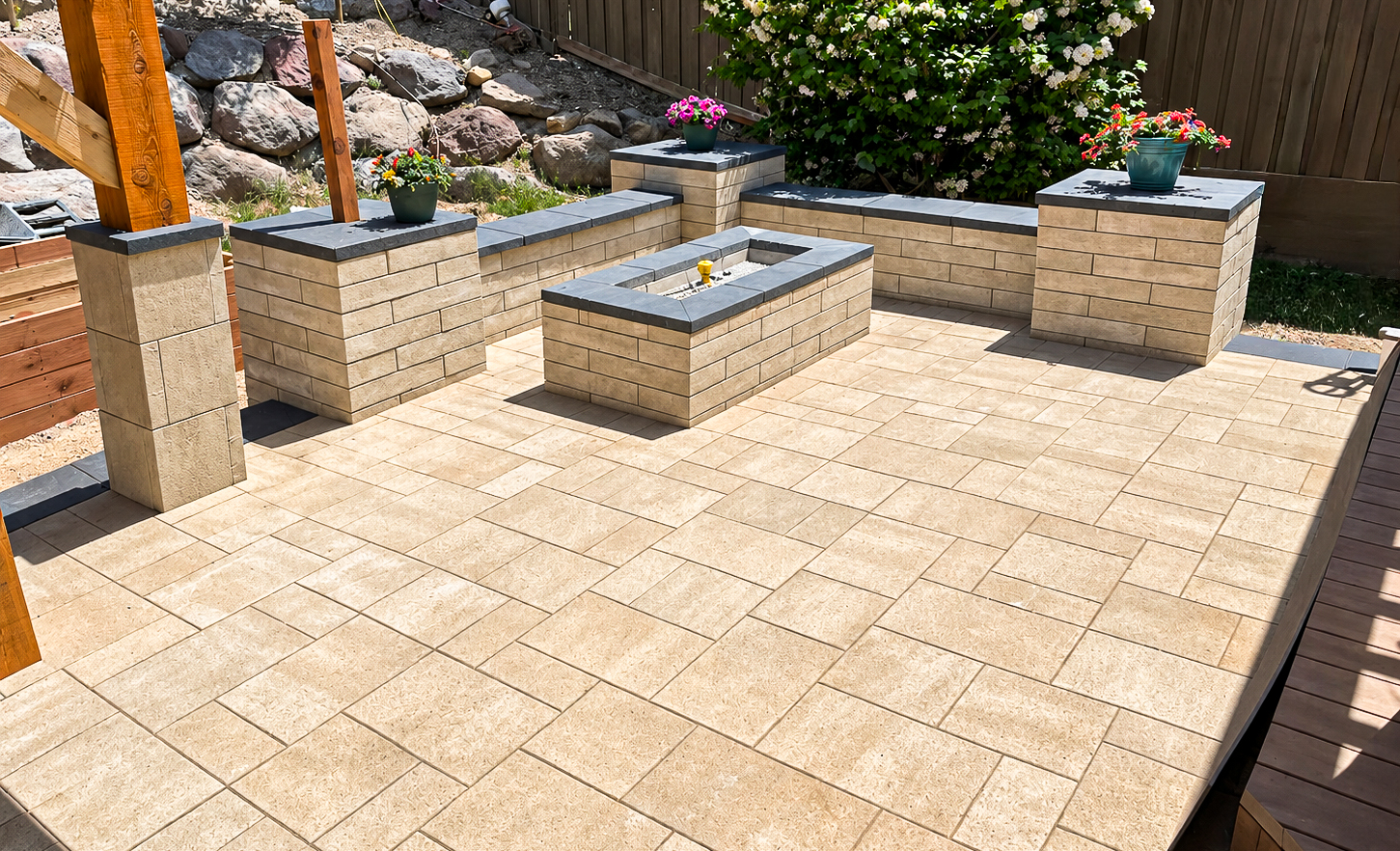 Custom Paver Patios in Utah Tan paver backyard patio with a matching stone fire pit, low retaining walls and potted flowers, custom paver patios by Empire Pavers in Utah